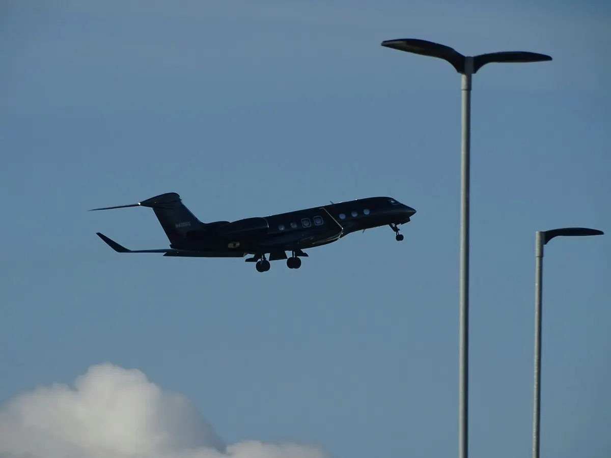 Small jet descending past lamp posts toward a runway